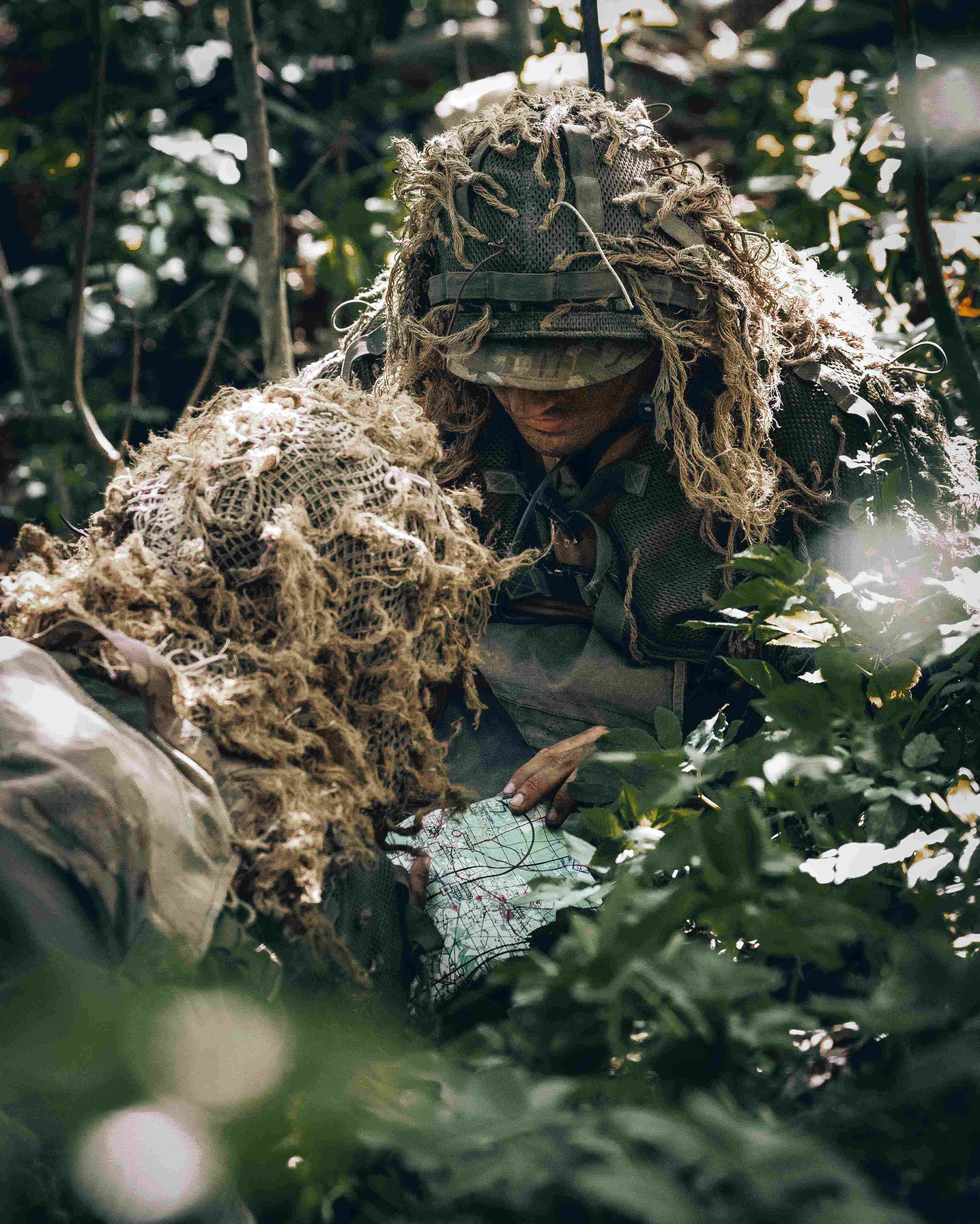 Two soldiers in a forest in camouflage reading a map 