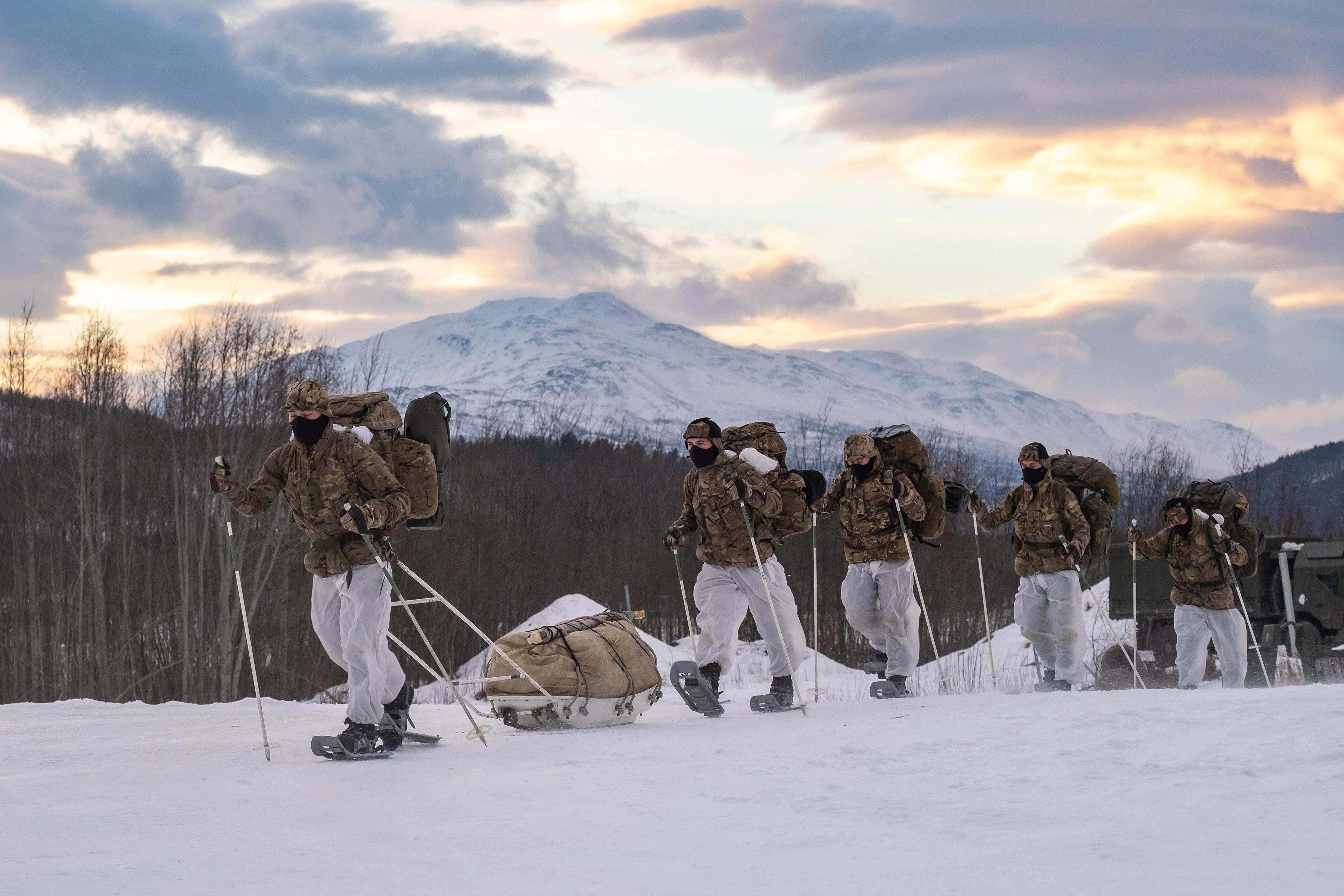 Group of soldiers marching in the snow with back packs, snow shoes and ski poles