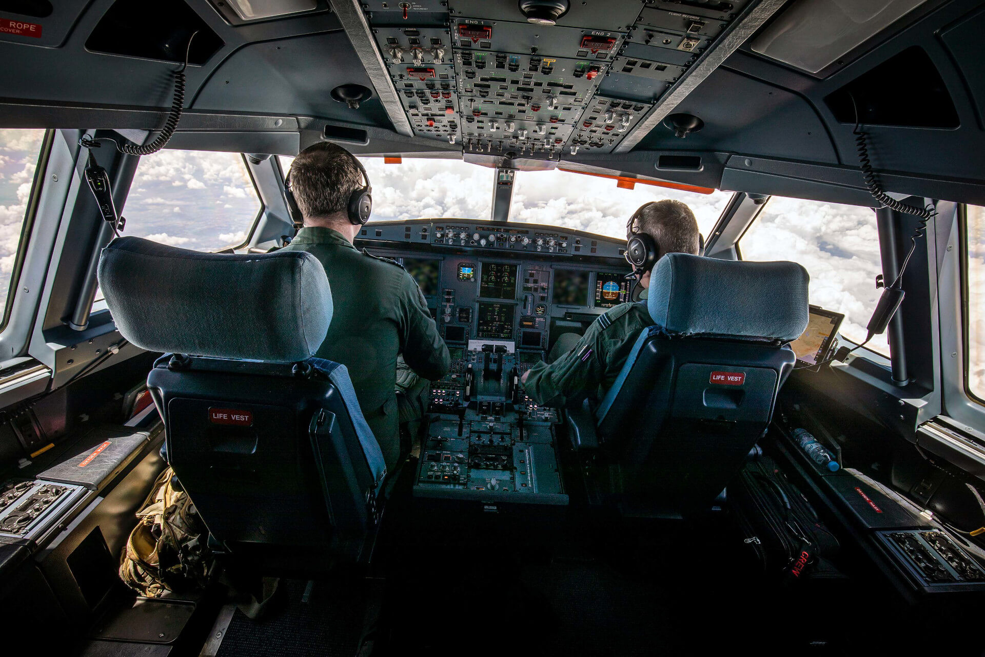 Two RAF pilots in green jumpsuits in cockpit of plane flying through the sky